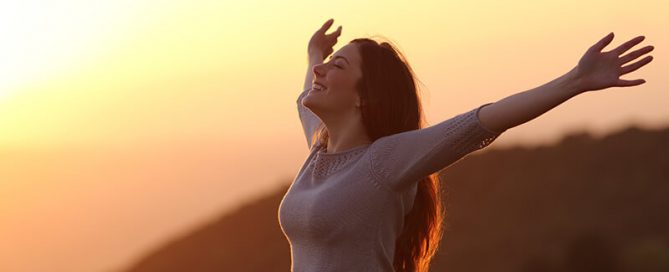 Woman at sunset breathing fresh air raising arms